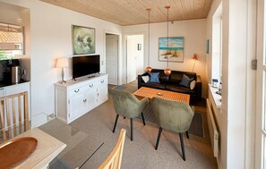 A modern living room with a flat-screen TV, white cabinetry, a black leather sofa, two green armchairs, a wooden coffee table, and artwork on the walls. - Amazing apartment in Borre with house sea view (Borre)