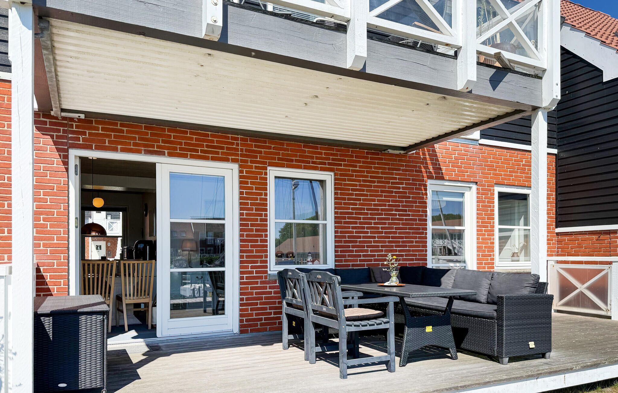 Une terrasse couverte avec des meubles d’extérieur, un bâtiment en briques et une porte de garage.