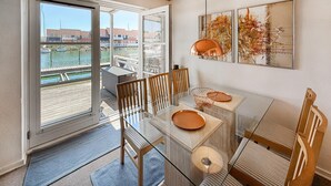 En matplats med ett glasbord, randiga stolar och utsikt över en vattenyta och byggnader.