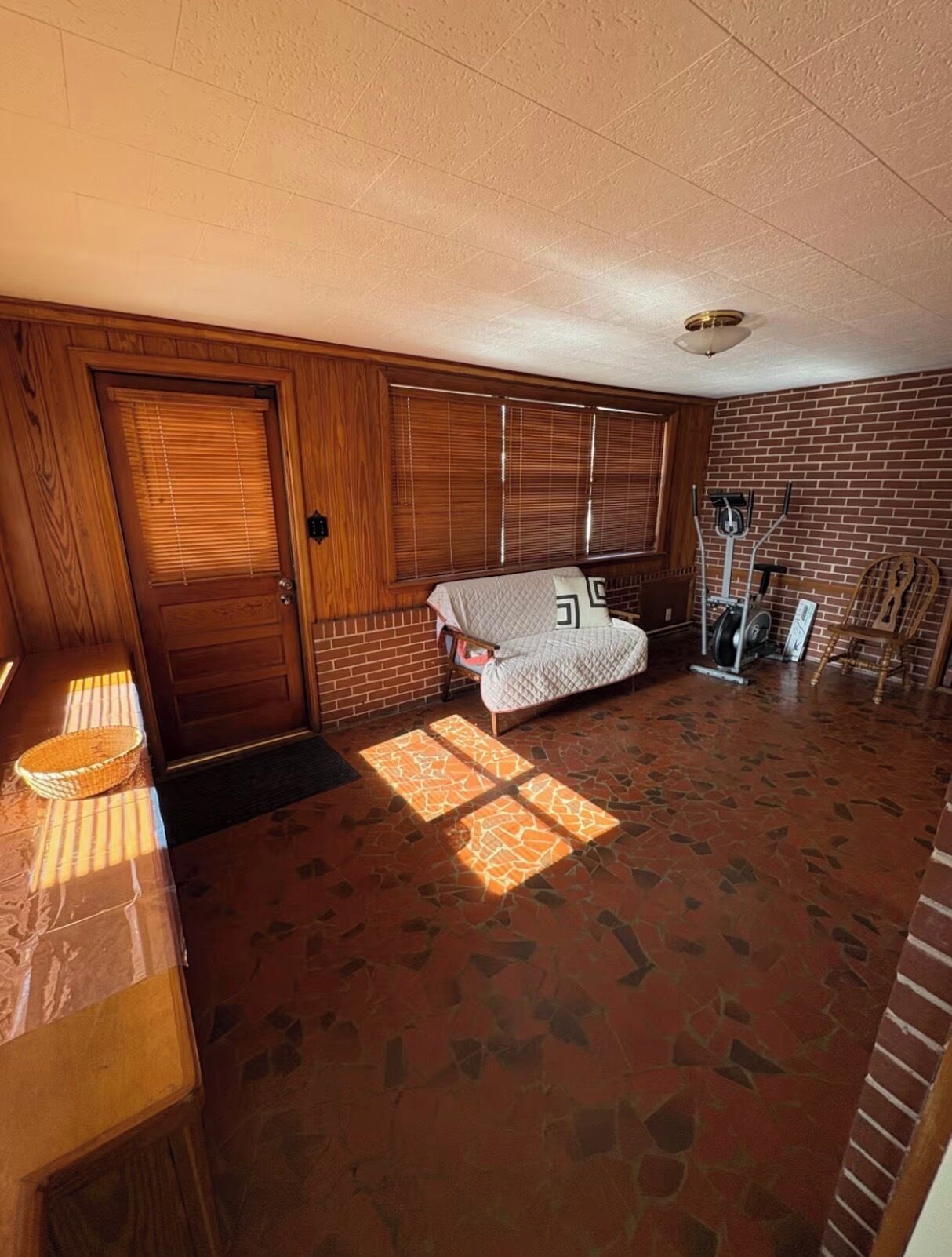 A room with a brick wall, a wooden door, a bed, and exercise equipment.