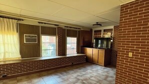 Una habitación amplia con suelo de baldosas, pared de ladrillo decorativa y ventana con cortinas.