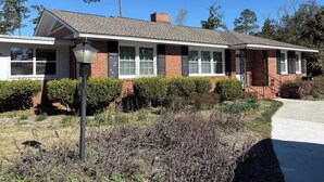 Una casa de dos pisos con fachada de ladrillo, ventanas blancas y un porche delantero.