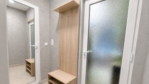 Un couloir avec un banc en bois, un porte-manteau et une porte en verre dépoli.