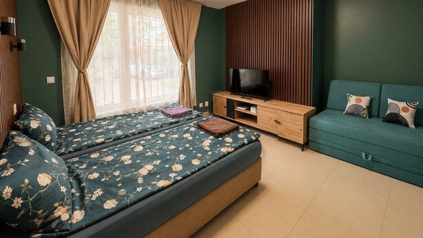 Une chambre à coucher avec un lit, une télévision, un canapé et une fenêtre avec des rideaux.