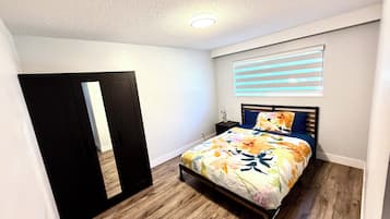Un dormitorio con cama, mesita de noche, lámpara, ventana con persianas y puerta.