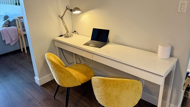 A white desk with a laptop, a desk lamp, and two yellow chairs.