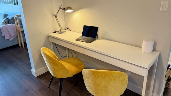 A white desk with a laptop, a desk lamp, and two yellow chairs.