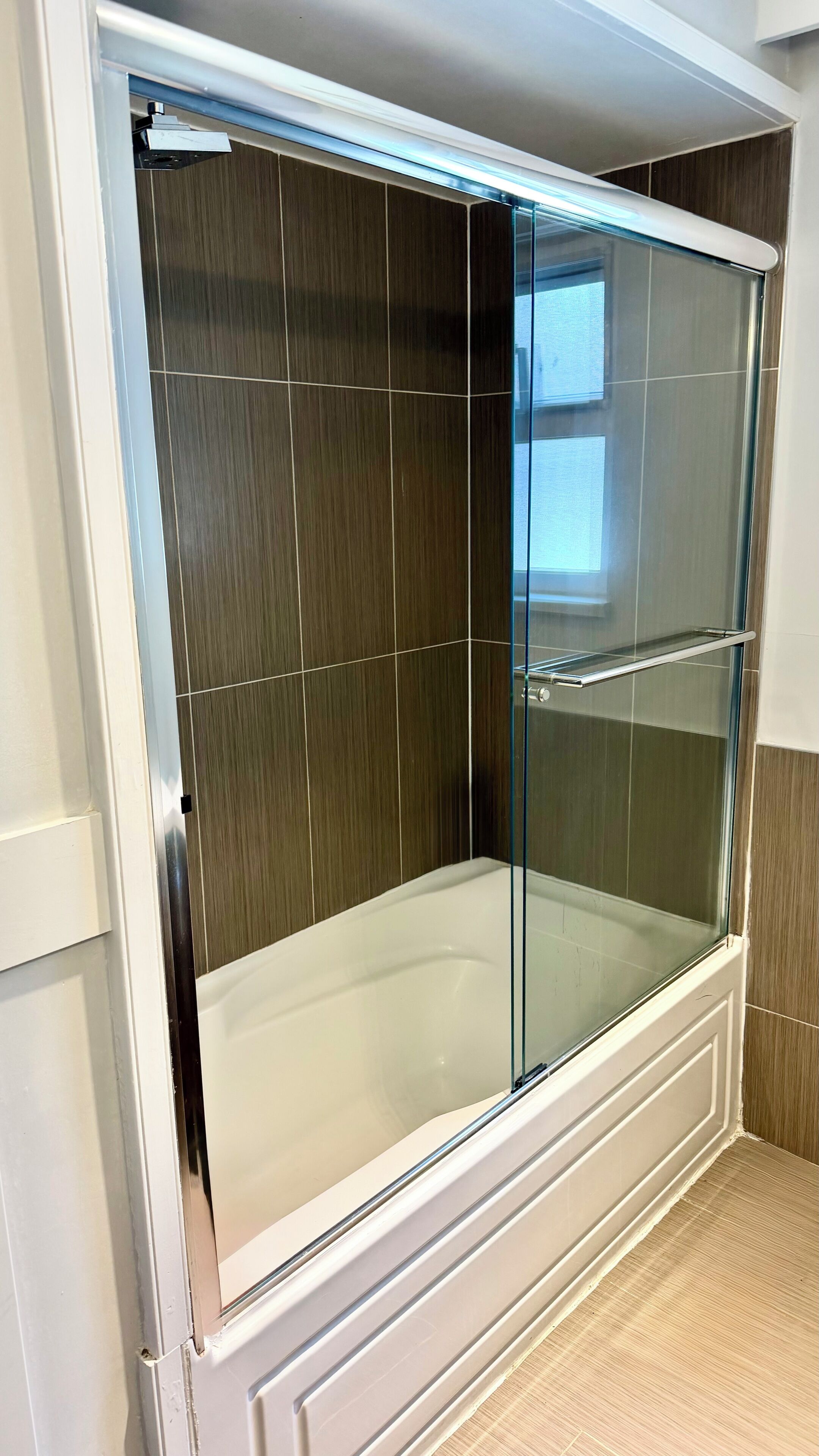 Une douche à l’italienne avec des parois en verre, une baignoire blanche, un lambris en bois sur les murs et une porte en verre.