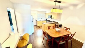 A compact kitchen with a dining area, including a wooden table and chairs, a small island with a microwave, and a hanging light fixture.
