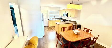 A compact kitchen with a dining area, including a wooden table and chairs, a small island with a microwave, and a hanging light fixture.