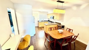A compact kitchen with a dining area, including a wooden table and chairs, a small island with a microwave, and a hanging light fixture.