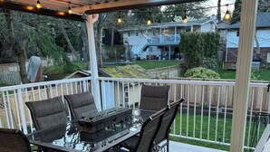 An outdoor patio with a glass enclosure, a table with chairs, and a grill.