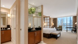 Ein Hotelzimmer mit Bett, Schreibtisch, Stuhl, einem großen Fenster und einem Badezimmer mit Spiegel und Waschbecken.