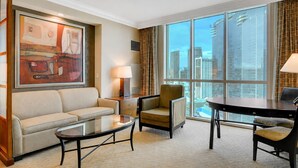 Ein Hotelzimmer mit großem Fenster, einer Couch, einem Sessel, einem kleinen Tisch und einem Gemälde.