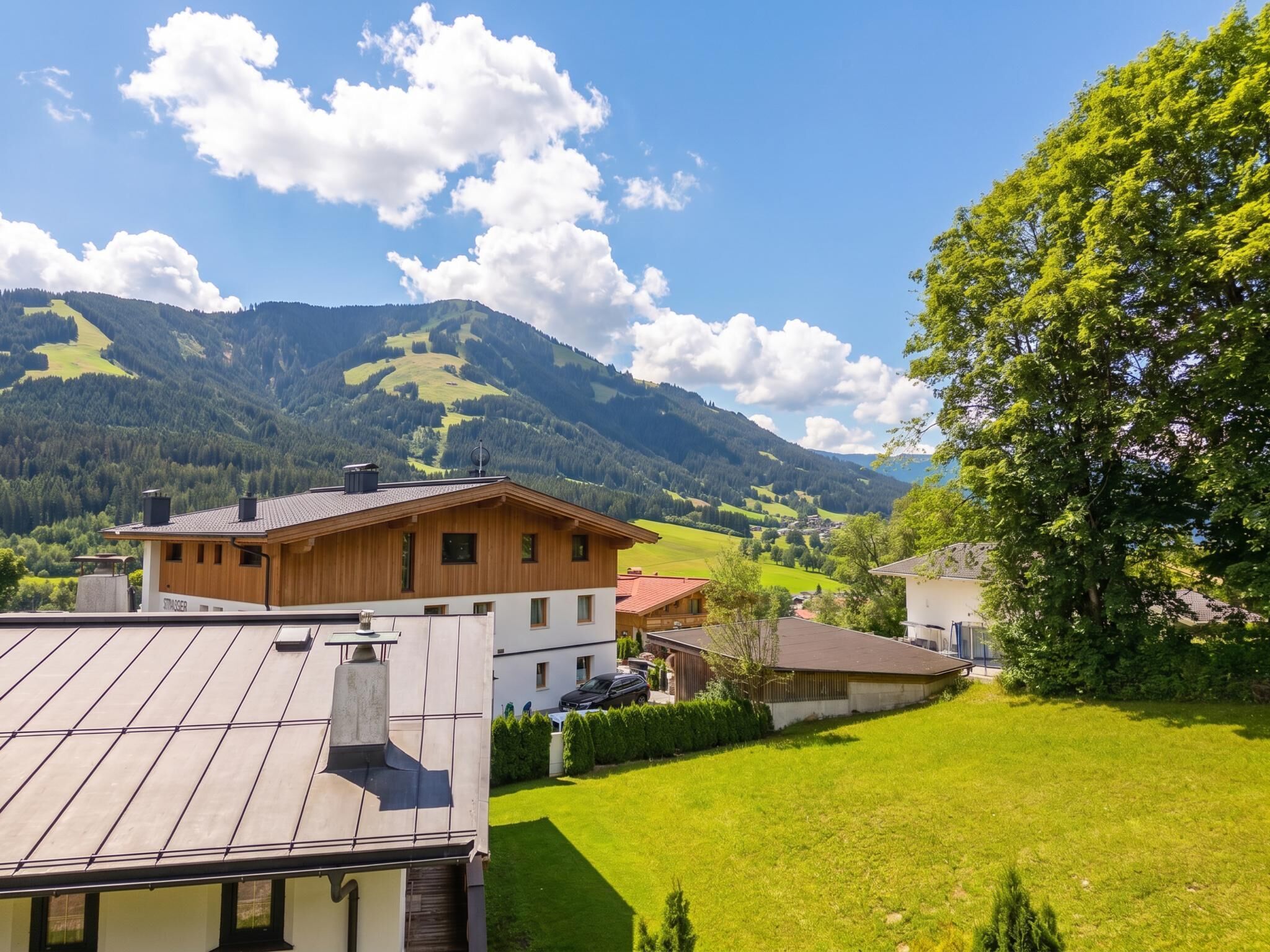 Un quartier résidentiel avec une maison en bois, un toit équipé de panneaux solaires et une vue sur des collines verdoyantes et des montagnes.