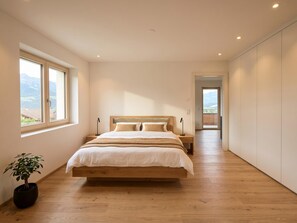 Un dormitorio con una cama de madera, una mesita de noche, una planta en maceta y vistas a las montañas a través de una ventana.