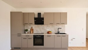 A modern kitchen with a central island, built-in oven, and a black faucet. - Stylish apartment with sauna, by the slopes (Brixen im Thale)