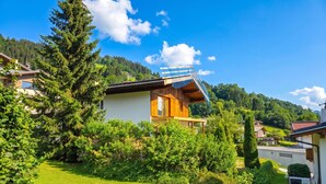 A modern house with a wooden deck, surrounded by lush greenery and a clear blue sky. - Stylish apartment with sauna, by the slopes (Brixen im Thale)