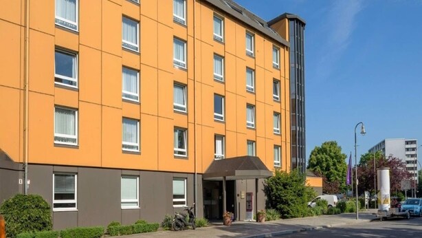 Un hotel de varios pisos con fachada plana, amplias ventanas y un acceso cubierto.