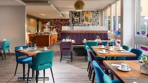 Un comedor moderno con mesas de madera y sillas color turquesa, una zona de bar central y un muro con diseño.