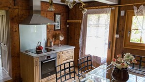 Interior de una cabaña de madera con cocina, una mesa de comedor, sillas y una ventana con cortinas.