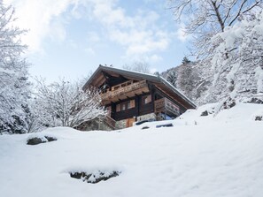 Eine Holzhütte mit einem Balkon, umgeben von schneebedeckten Bäumen und blauem Himmel.