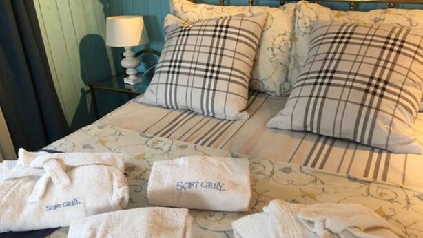 Una cama con ropa de cama escocesa y múltiples toallas con la marca 'Soft Grey'.