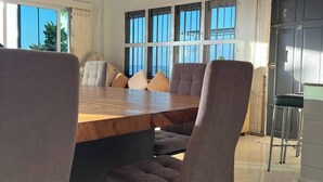 A dining area with a wooden table and cushioned chairs, large windows, and a view of the outdoors.