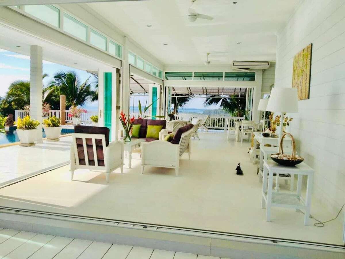 A spacious indoor area with white furniture, a view of the ocean, and a ceiling fan.
