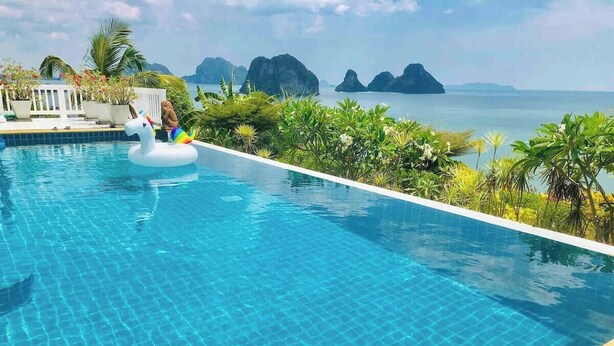 A swimming pool with a unicorn float, surrounded by tropical plants and a view of the sea.