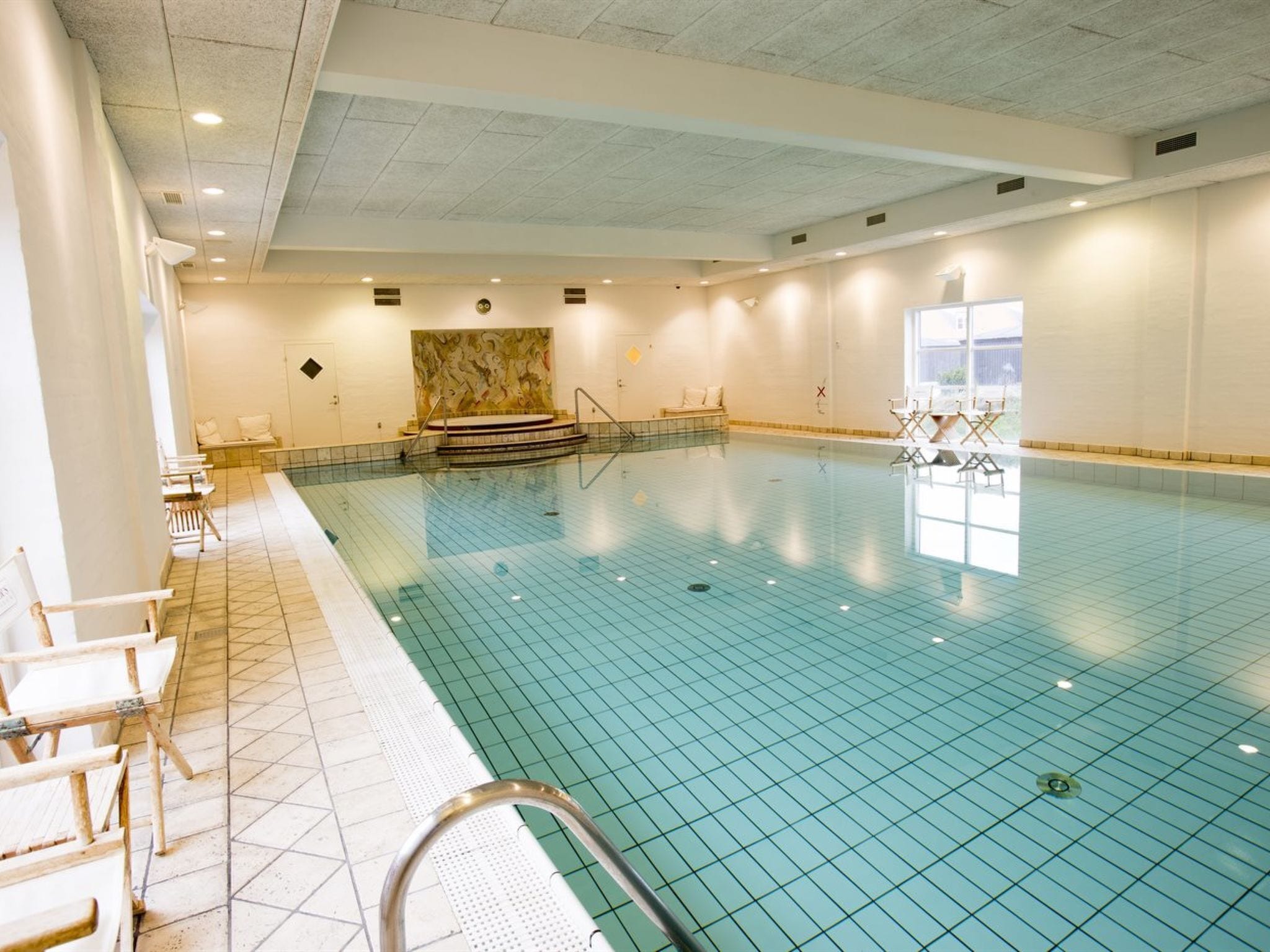 Une piscine dont le fond est recouvert de carrelage, avec un banc et une chaise situés à proximité du bord.
