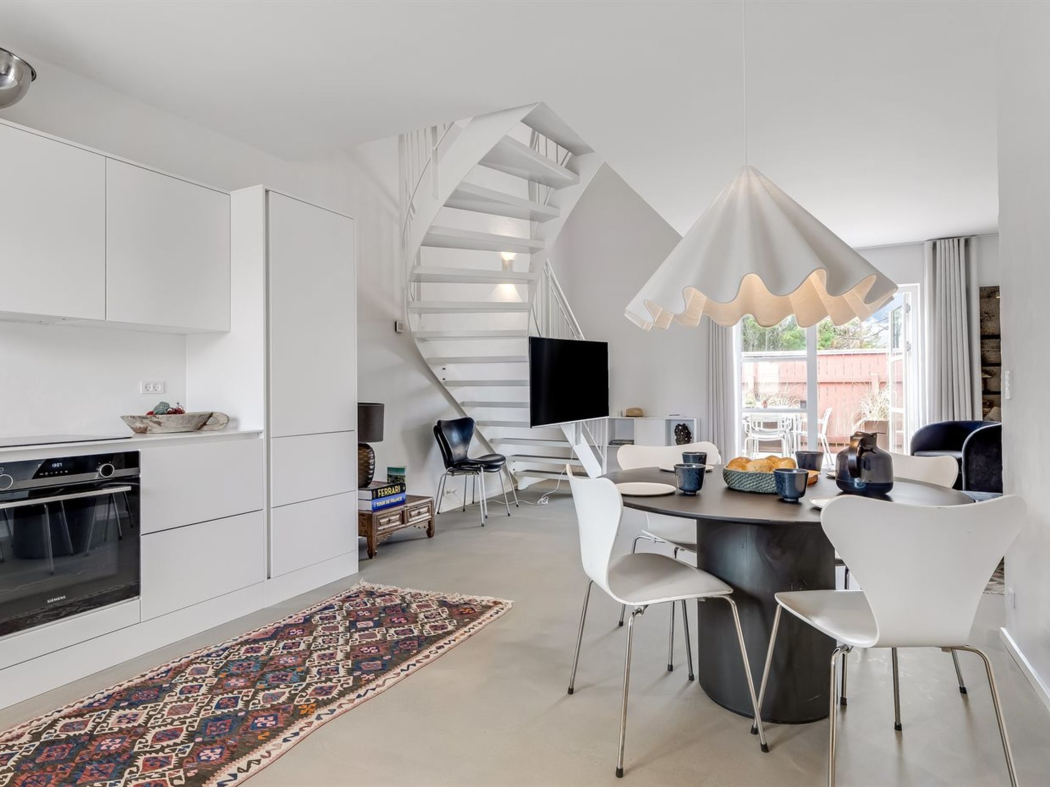 A modern kitchen with white cabinetry, a built-in oven, and a dining area with a round table and chairs.
