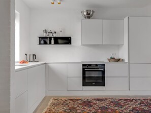 A modern kitchen with white cabinetry, a built-in oven, a coffee maker, and a hanging light fixture. - "Ehlin" - 900m from the sea by Interhome (Skagen)