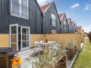 Un bâtiment moderne à la façade sombre, doté d’un patio couvert avec des sièges extérieurs et d’un barbecue.