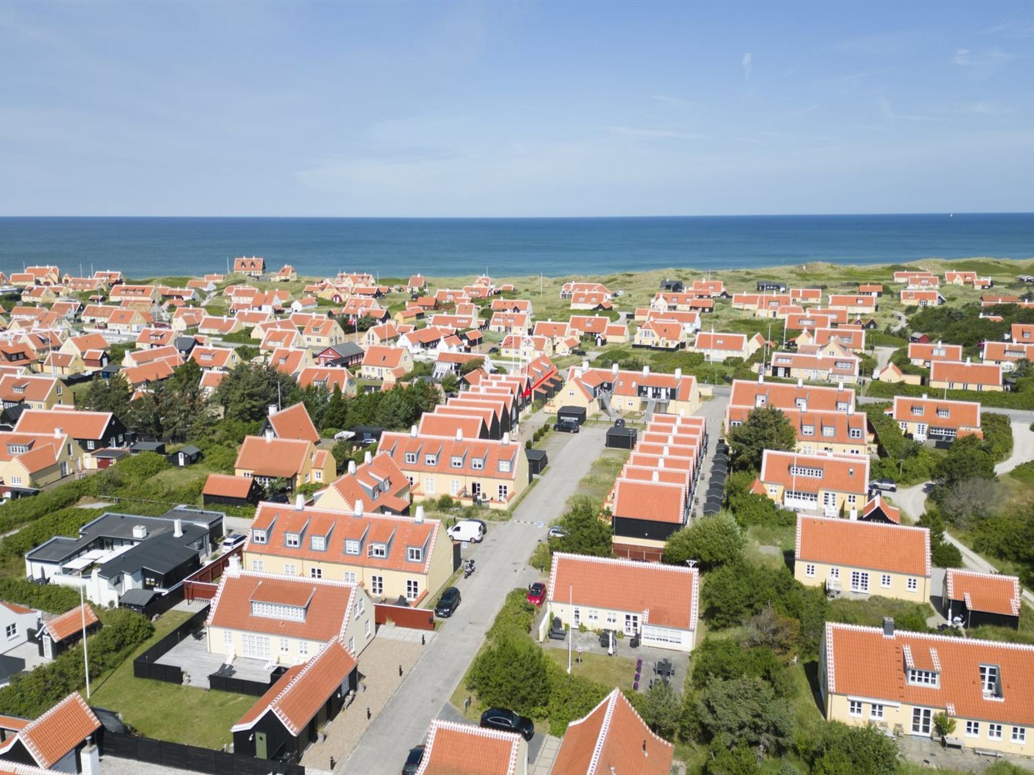 Une zone résidentielle côtière où les maisons sont toutes identiques, le ciel est dégagé et l’océan se profile à l’horizon.
