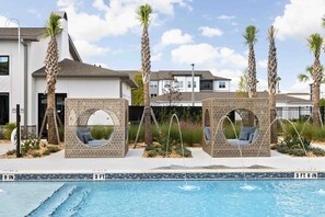 Una piscina con due lettini circolari, palme e un edificio moderno sullo sfondo.