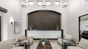 Un área de recepción con un fondo de madera oscura, un separador de vidrio y asientos con plantas.