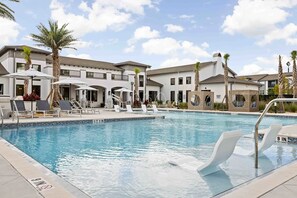 A swimming pool with lounge chairs and umbrellas, surrounded by buildings with balconies and palm trees. - Lux resort Apartment St Augustine Baptist Wolfson UF Hospital Pool Gym (St. Augustine)