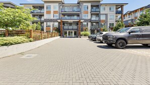 Um edifício residencial de vários andares com um caminho pavimentado e veículos estacionados.