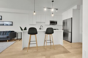 A modern kitchen with white cabinets, a stainless steel refrigerator, and a bar area with two stools. - Spacious 1BR + Office in Central Langley (Langley Township)
