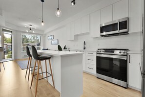 Una cocina moderna con armarios blancos, una isla central con taburetes, horno empotrado y microondas.