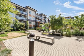 A residential complex with multiple apartment buildings, a playground, and a paved courtyard with benches. - Spacious 1BR + Office in Central Langley (Langley Township)