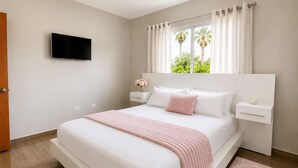 A bedroom with a bed, a TV, a nightstand, a window with curtains, and a view of greenery outside.