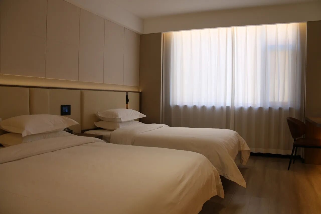 Une chambre d’hôtel avec deux lits, une table de chevet, une chaise et une grande fenêtre avec des rideaux.