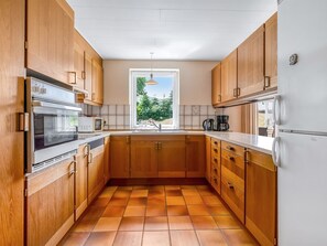 Eine Küche mit Holzschränken, einem Fenster, einem eingebauten Backofen und einem Kühlschrank.