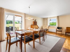 Ein Essbereich mit einem Tisch für vier Personen, einer Holzkabine und Blick durch eine Glastür in einen Außenbereich.
