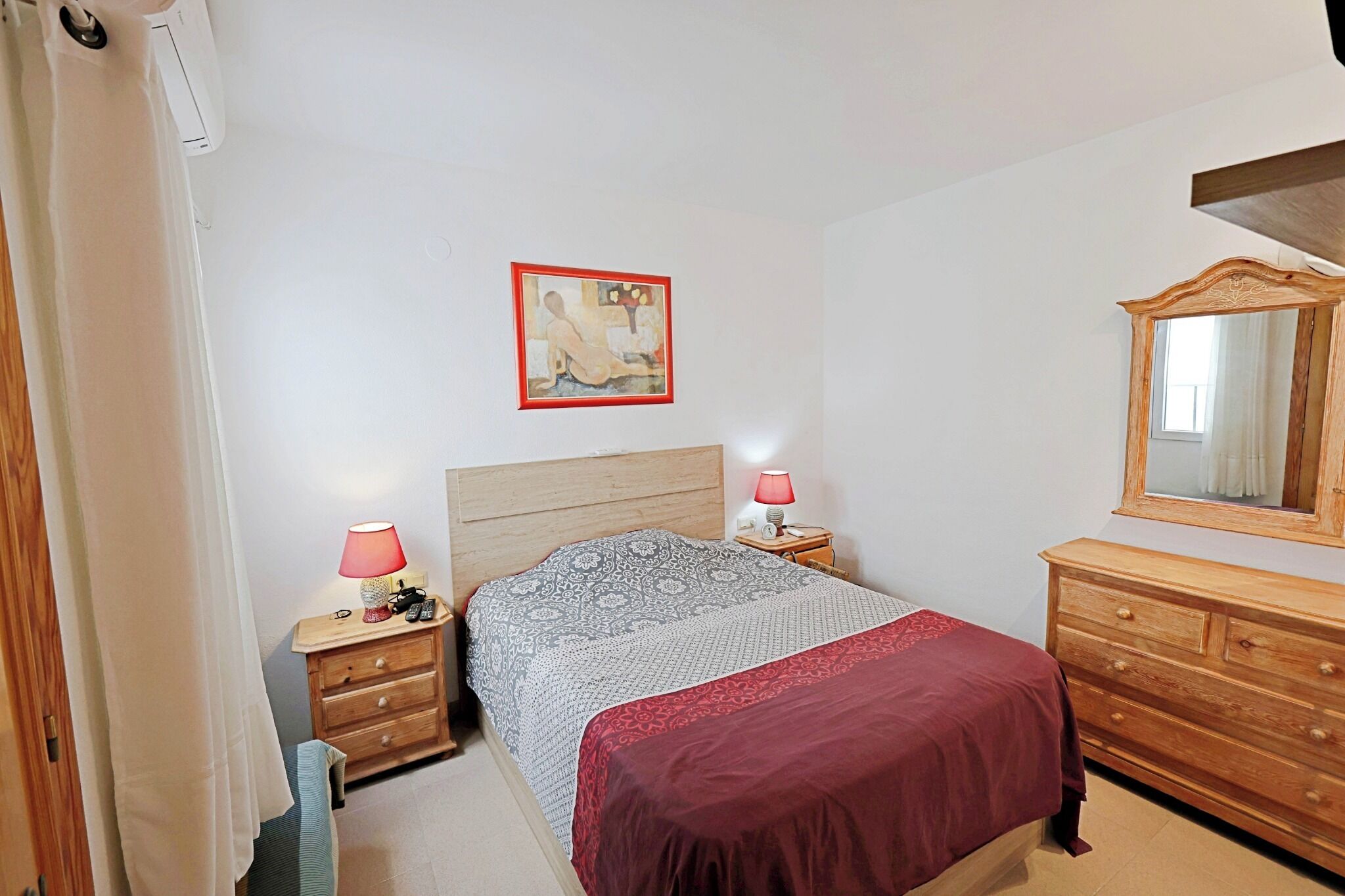 A bedroom with a bed, bedside tables, a dresser, a mirror, and a painting on the wall.