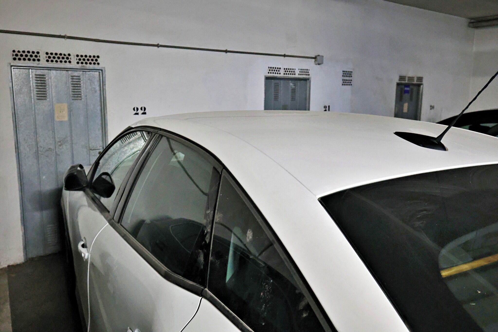 A white car parked in a garage with lockers and an elevator.