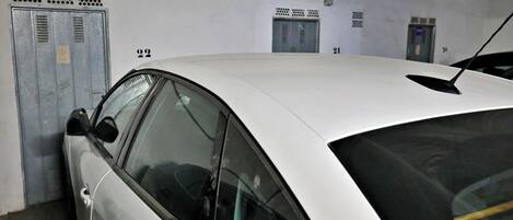 A white car parked in a garage with lockers and an elevator.