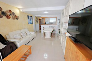 A living room with a sofa, a coffee table, a TV, and a kitchen area with cabinets and a sink. - Sabine - apartment located in the heart of Calpe (Calpe)